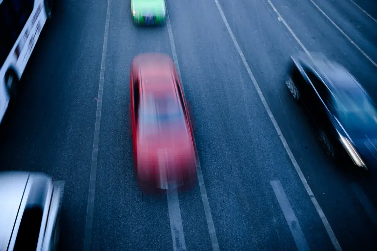 Aerial view of fast-moving cars on a multi-lane highway, with motion blur emphasizing speed, featuring a red car in focus.