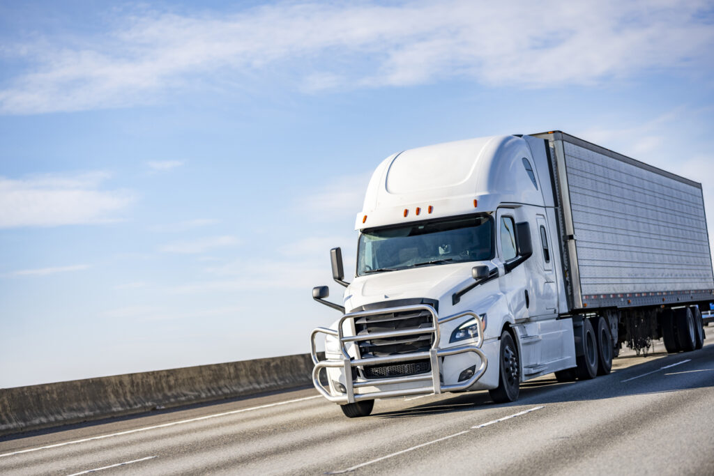Commercial big rig white industrial long haul semi truck transporting frozen cargo in refrigerator semi trailer driving on the multiline interstate highway road with one way traffic direction