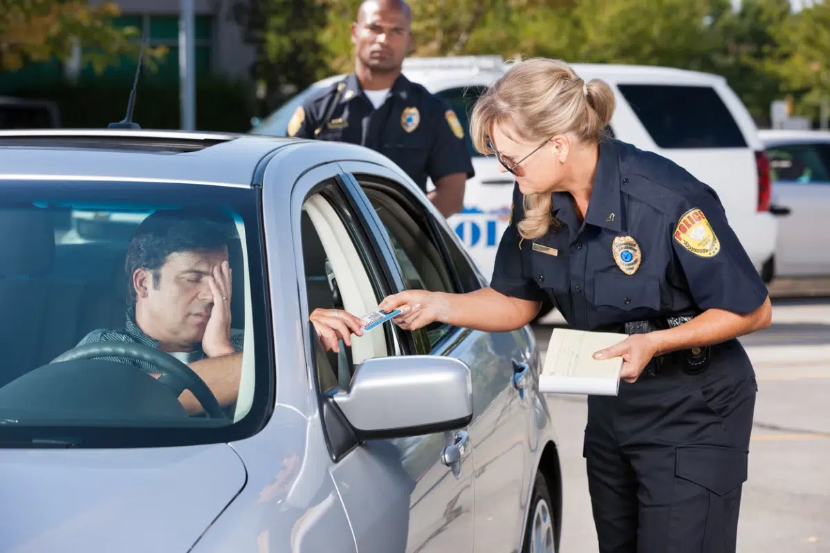 Female police officer checking driver's license during a traffic stop, with a second officer standing nearby.